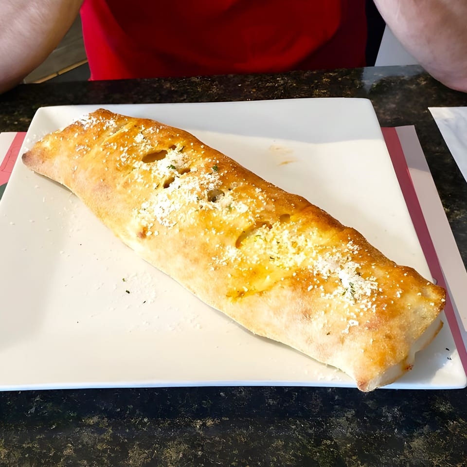 A golden-brown calzone, sprinkled with parmesan cheese, rests on a white rectangular plate at Luca Trattoria & Pizzeria.