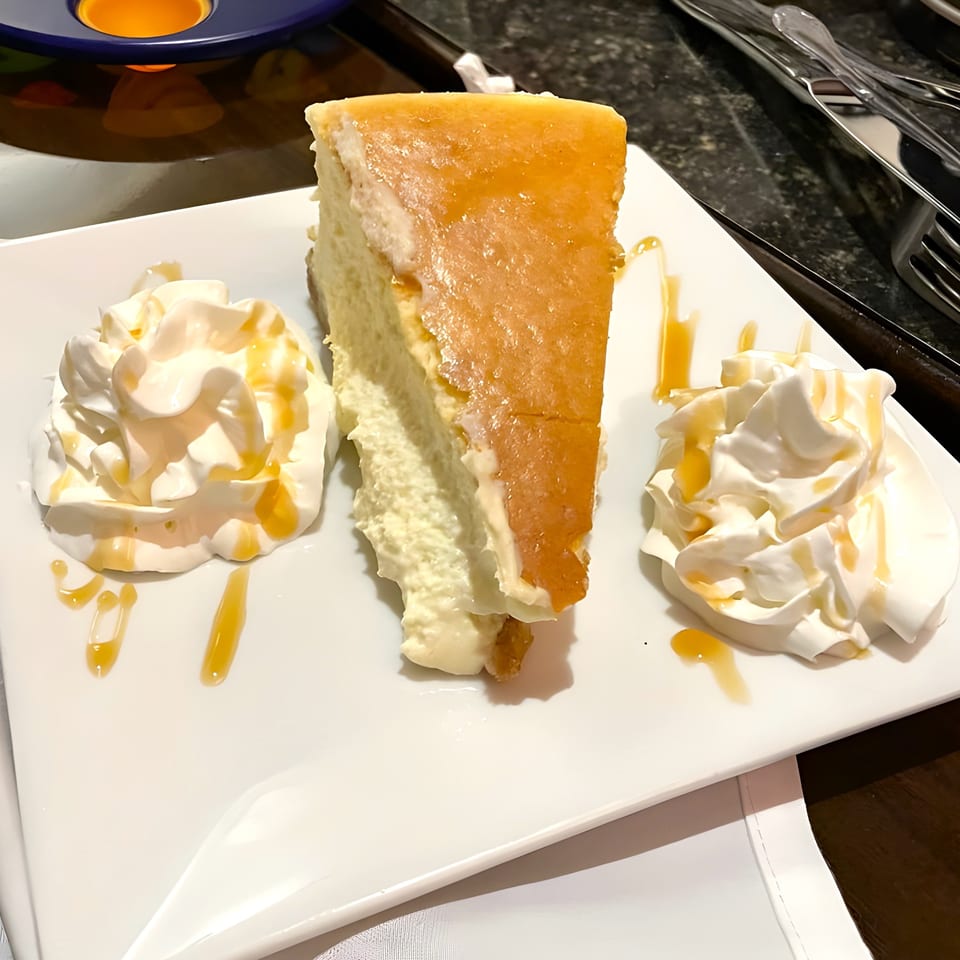 Slice of cheesecake with caramel drizzle and two dollops of whipped cream on a white plate.
