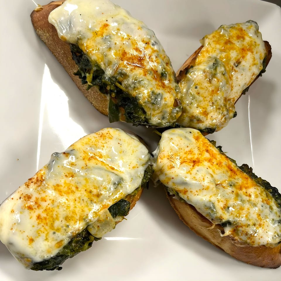 Four cheesy spinach and artichoke bread appetizers, arranged in a cross on a white plate.