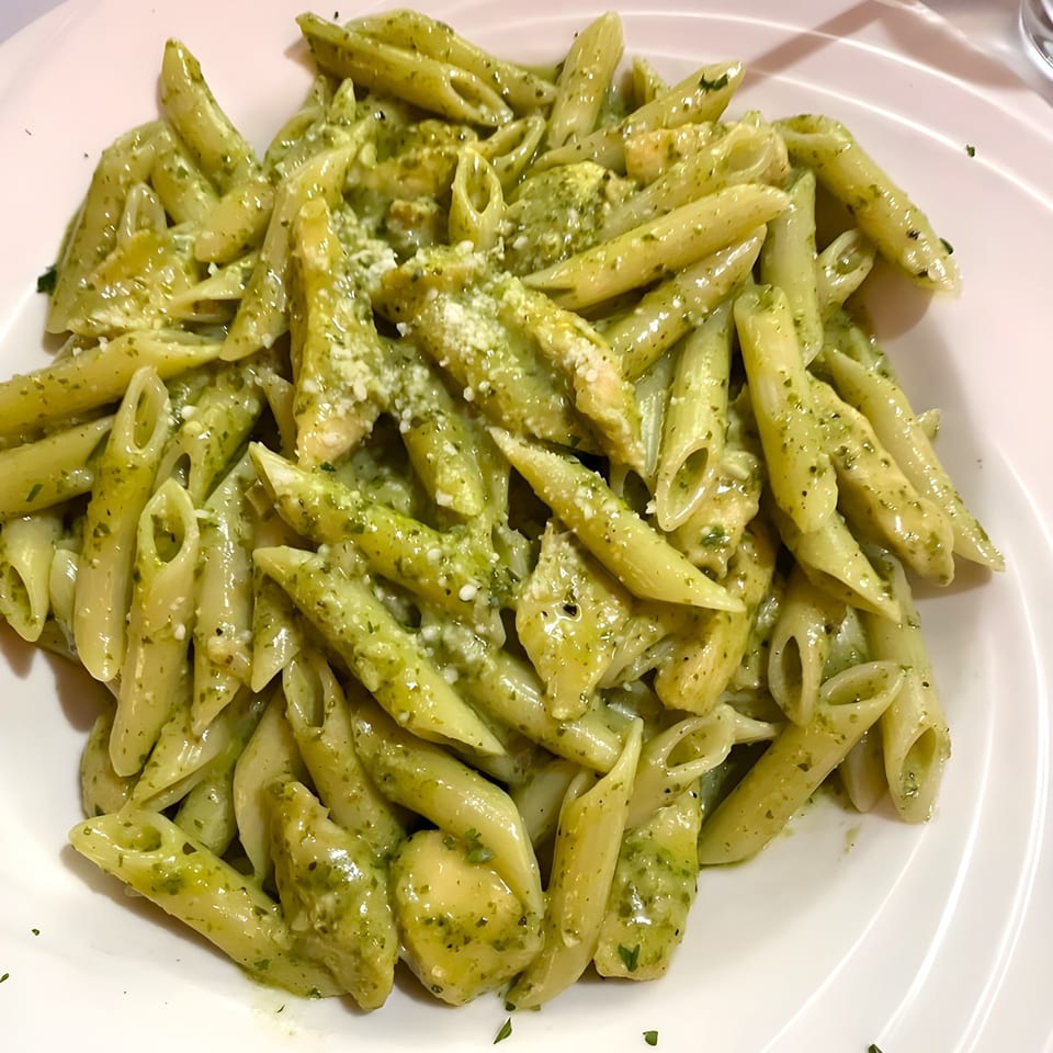 Penne pasta with vibrant green pesto sauce and grated cheese on a white plate at Luca Trattoria.